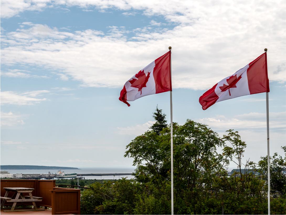 Two canadian flags on flag poles overlooking a scenic view