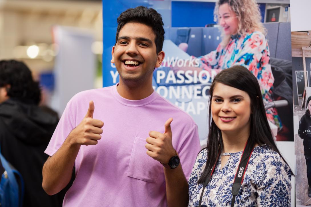 Two people smiling at a job fair giving a thumbs up